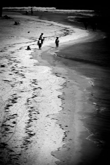 Deux personnes marchent le long d'une plage déserte, avec des vagues au loin.