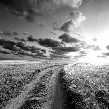 Chemin sinueux à travers un paysage vaste sous un ciel nuageux et lumineux.