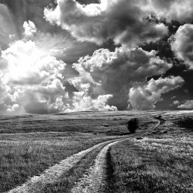Paysage en noir et blanc avec un chemin sinueux sous un ciel nuageux.