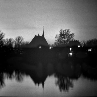 Silhouette d'un paysage avec un bâtiment et des arbres au bord d'un étang nocturne.