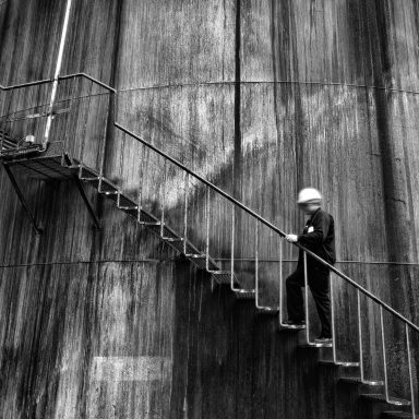 Un ouvrier en casque descend un escalier métallique face à un mur texturé.