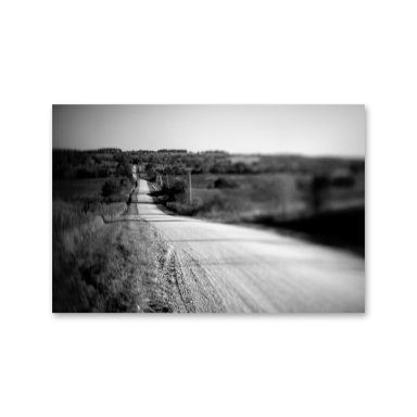 Route sinueuse à travers un paysage rural, en noir et blanc.