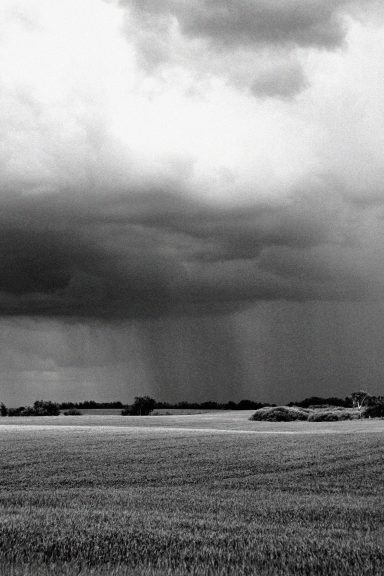 Ciel nuageux avec des pluies sur un paysage de campagne en noir et blanc.