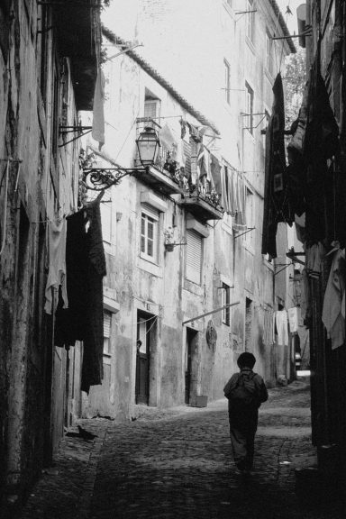 Un enfant marche dans une ruelle étroite entre des bâtiments, avec des vêtements suspendus.