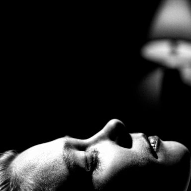 Femme au visage serein, éclairée par une lampe dans une ambiance sombre.