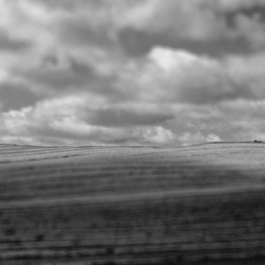 Paysage en noir et blanc avec des champs ondulés et des nuages dans le ciel.