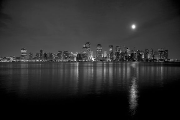 Vue nocturne en noir et blanc d'une ville avec un ciel étoilé et le reflet sur l'eau.